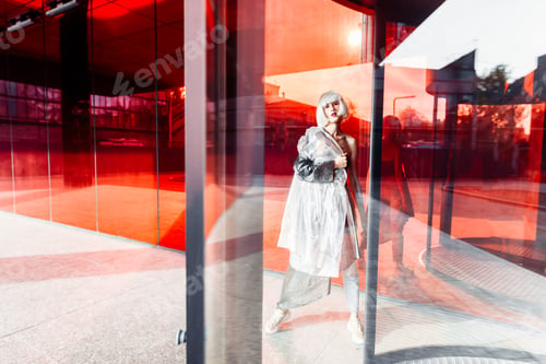 Preview: Young stylish woman standing near a red modern building.