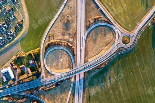 Preview: Aerial top view of modern highway road intersection, house roofs on spring green field