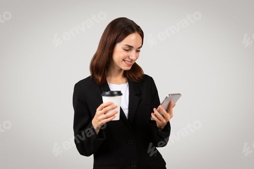 Preview: Multitasking businesswoman in a smart black suit happily checks her smartphone