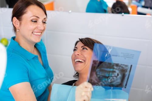 Preview: Close up female dentist pointing at patient's X-ray image in dental office.