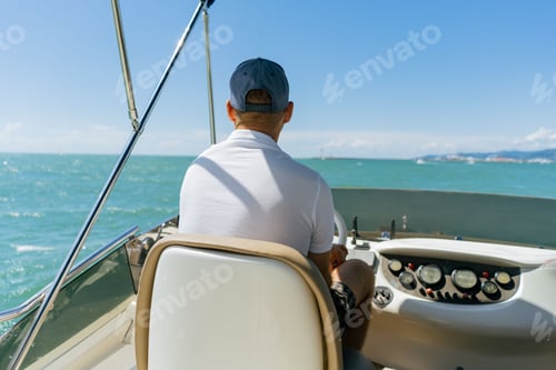 Preview: Bach view of middle-aged man driving luxury motor yacht. Captain at the helm of motor boat.