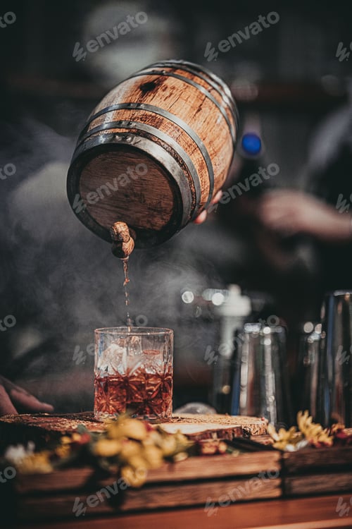Preview: Vertical shot of a hand holding a cask and pouring a beverage in the glass on the bar counter.
