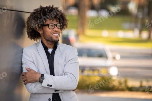 Preview: Positive black businessman in suit posing by office center, having break after successful business