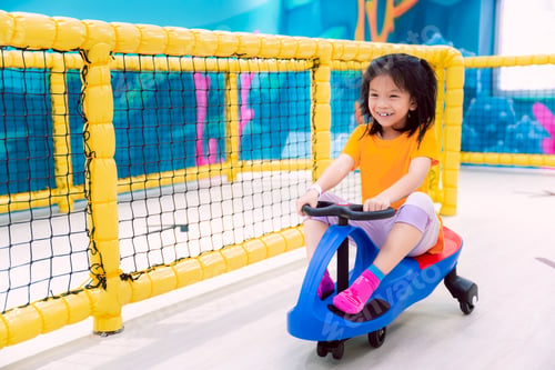 Preview: Adorable Asian child girl riding blue toy car in a indoor playground, smiling and having fun.