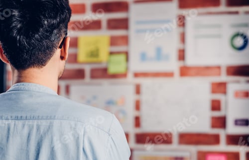 Preview: Asian man creative director designer looking at data chart and find idea on brickwall