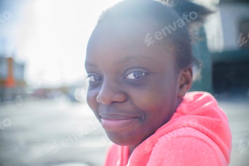 Preview: Portrait of teenage girl wearing pink hoody on urban sidewalk