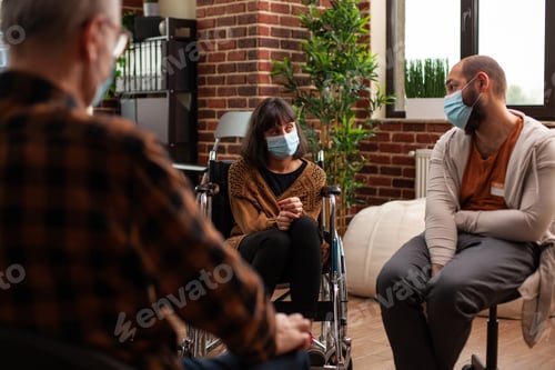 Preview: Woman with face mask sitting in wheelchair at group therapy session