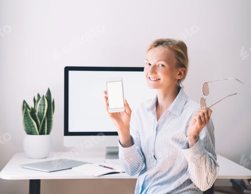 Preview: Woman shows smartphone with empty white display at office indoor.