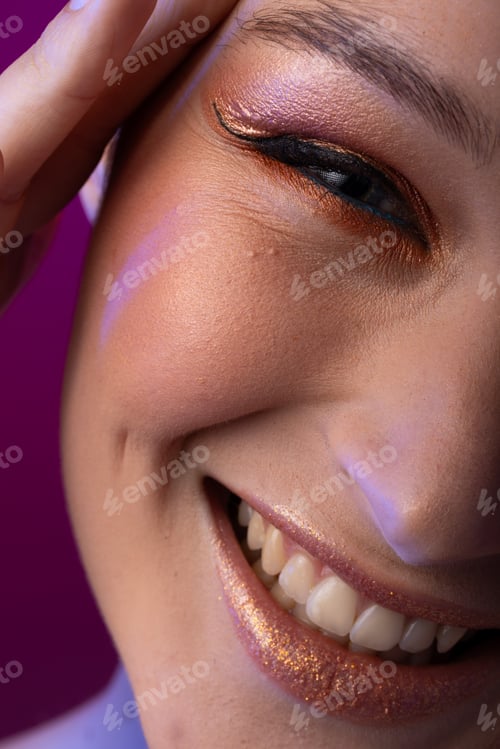 Preview: Portrait of caucasian woman wearing golden eye shadow and lipstick on purple background