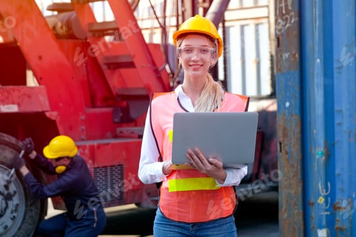 Preview: Beautiful technician or worker woman in cargo shipping area work with laptop