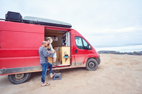 Preview: couple looking at a map together next to camper trailer on the beach