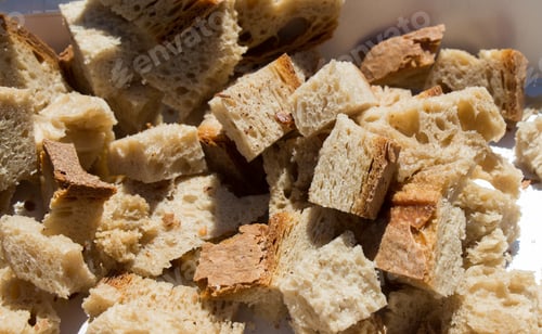 Preview: Closeup shot of cut-up and cubed bread on a white plate during daylight