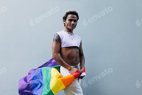 Preview: Young guy with LGBT flag posing at grey wall outdoors