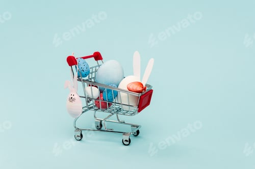 Preview: Colorful easter eggs and decorative rabbits in cart on blue background