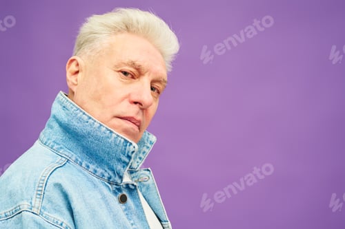Preview: Serious aged man with white hair in blue denim jacket looking at camera