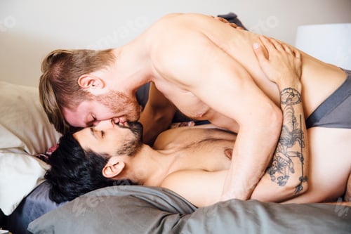 Preview: Male couple, partially dressed, lying on bed, kissing