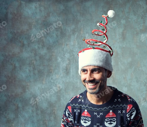 Preview: dark guy with short gray beard smiling in blue christmas sweater and funny christmas hat