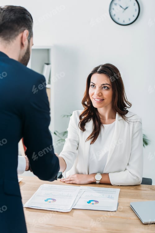 Preview: selective focus of beautiful advisor shaking hands with investor at workplace