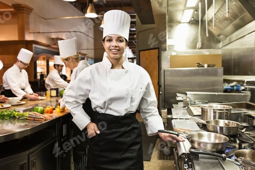 Preview: A portrait of a young black female chef in a commercial kitchen with her crew working behing her.