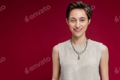 Preview: pleased young woman in sleeveless shirt and chain necklace standing on maroon background