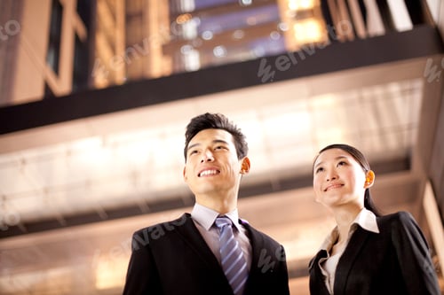Preview: A Chinese businessman and businesswoman outside an office building at night