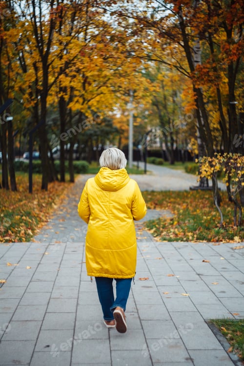 Preview: blonde woman in yellow coat walking at the autumn park