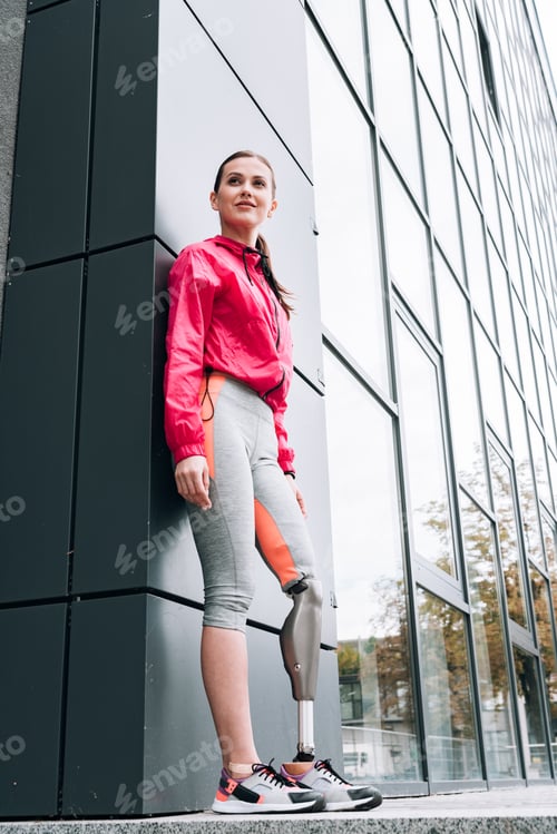 Preview: low angle view of smiling disabled sportswoman with prosthesis on street