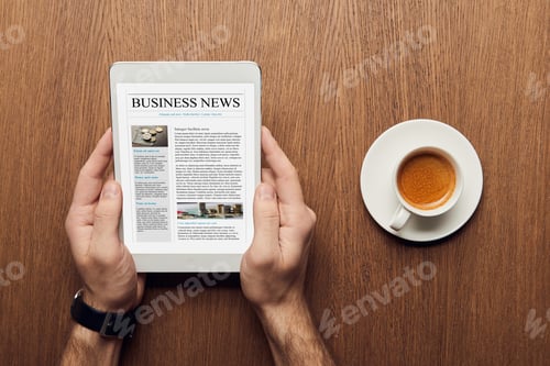 Preview: top view of man holding digital tablet with business news on screen near cup of coffee