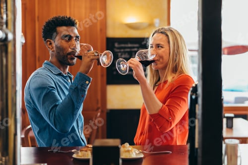Preview: multiethnic couple look at each other with feeling while drinking red wine from their glasses