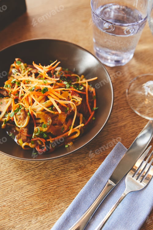 Preview: Plate with udon noodles and pork with cutlery on table