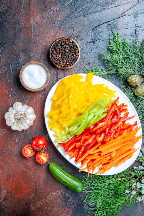 Preview: top view colorful cut peppers on plate salt and black pepper tomatoes garlic cucumber on dark red