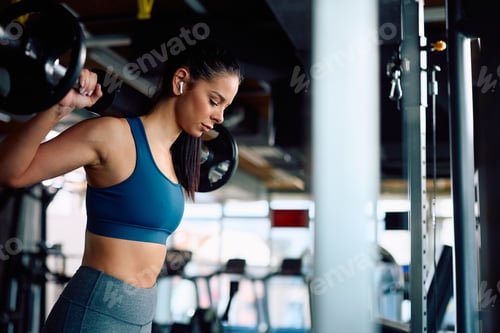 Preview: Athletic woman using barbell during weightlifting training in a gym.