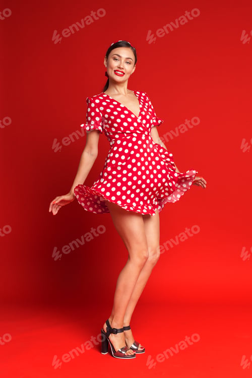 Preview: Woman poses in playful polka dot dress against bright red background
