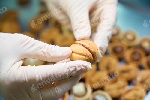 Preview: Qualified baker pressing together halves of shortbread sweet nuts with filling inside