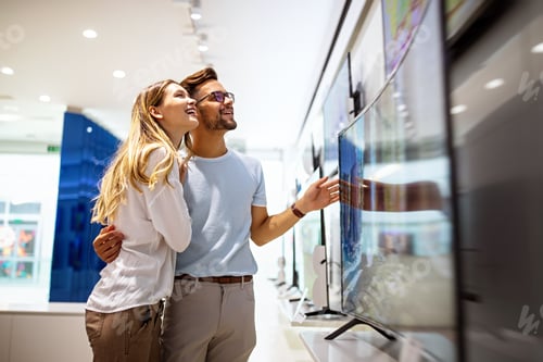 Preview: Young couple in consumer electronics store looking at latest digital devices, television.