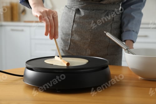 Preview: Woman cooking delicious crepe on electrical pancake maker in kitchen, closeup