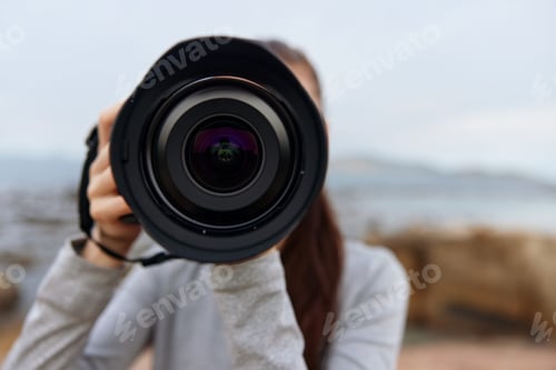 Preview: Young woman capturing nature with a camera, wearing casual gray clothing, conveying enthusiasm and