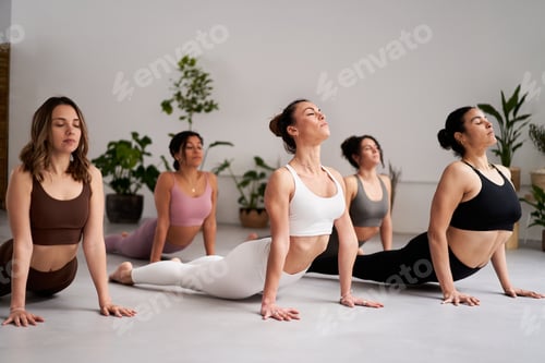 Preview: Group of women in a yoga class practicing downward-facing dog pose inside studio. Mental healthcare.