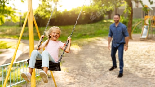 Preview: Family day. Happy girl swinging on swings having fun with father on playground, panorama, selective