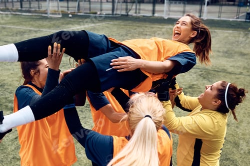 Preview: Cheerful soccer players carrying their teammate while celebrating after the match.