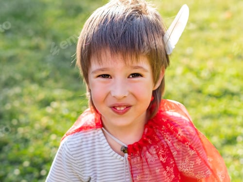 Preview: Portrait of smiling boy playing American Indian. Kid with white bird feather and red cloak.