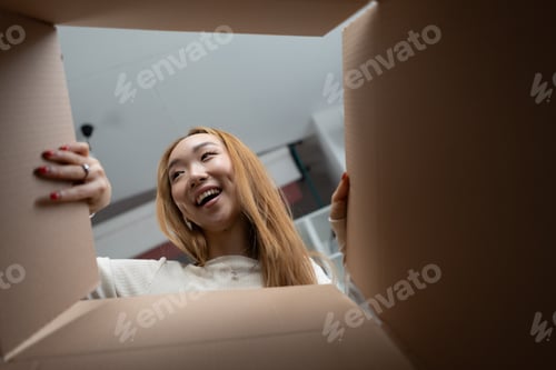 Preview: Happy Young Woman Excitedly Looks Into Cardboard Box