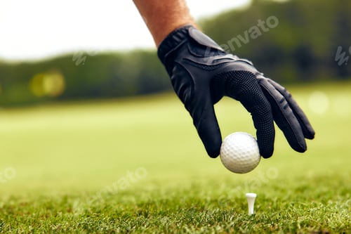 Preview: A CloseUp of a Golfer Intently Preparing to Tee Off with a White Golf Ball in Hand