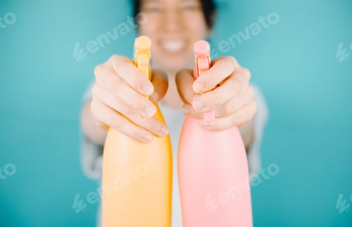 Preview: Young woman smiling happily to camera while aiming to camera a pair of water sprayer