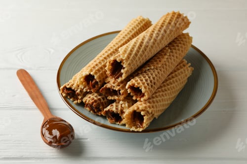 Preview: Plate with wafer rolls with condensed milk and spoon on wooden background