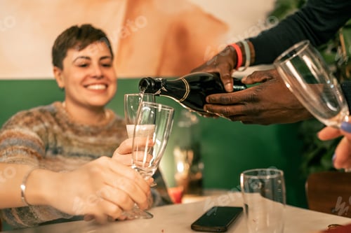 Preview: Close-up of hands pouring sparkling wine into a glass during a festive toast.