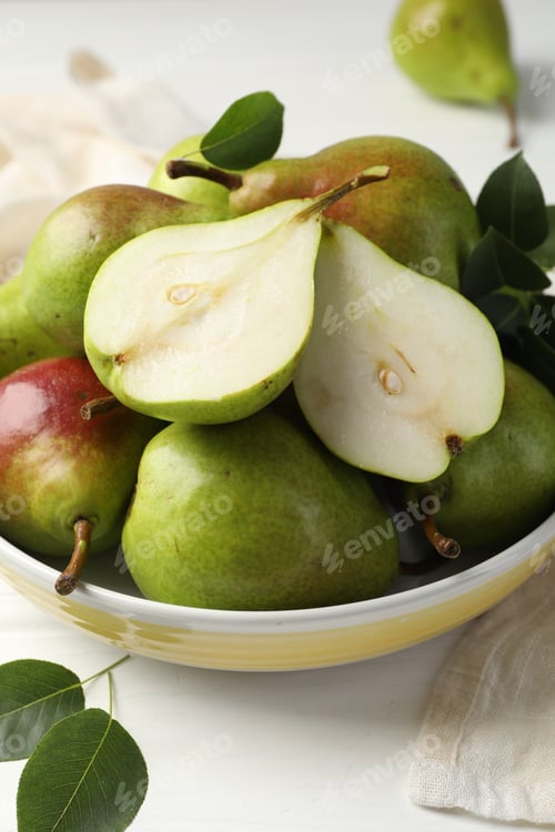 Preview: Fresh ripe pears in bowl and green leaves on white wooden table, closeup