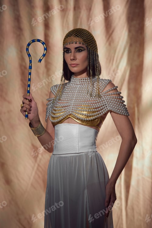 Preview: Elegant woman in egyptian look and pearl top holding traditional crook on abstract background