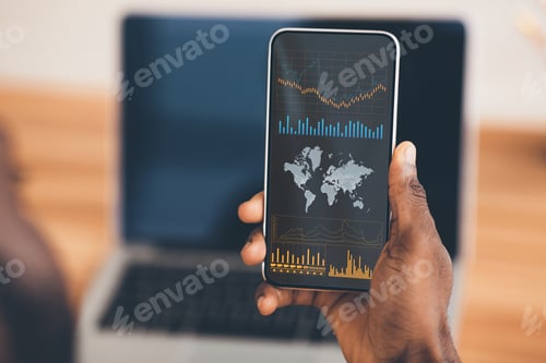 Preview: Mobile Trading. Black Businessman Holding Smartphone With Stock Market Data On Screen