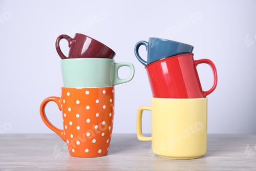 Preview: Many colorful cups on light wooden table against white background, closeup